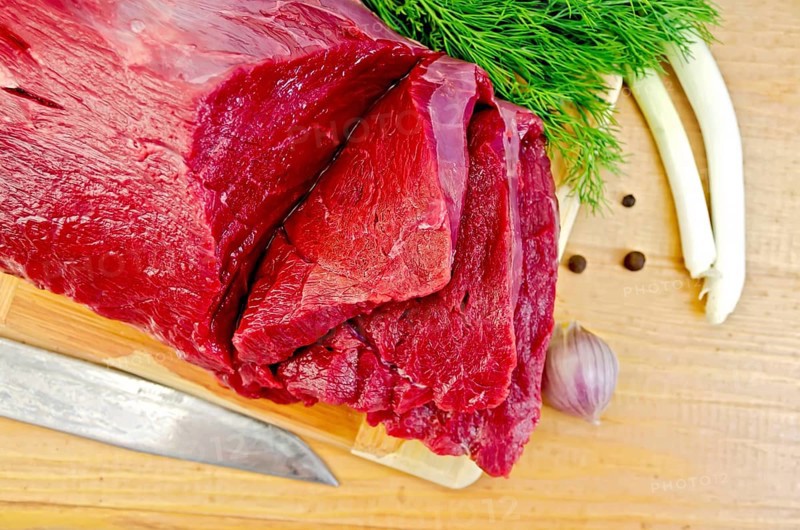 A piece of beef, garlic, peas pepper, dill, chives, knife on a wooden board