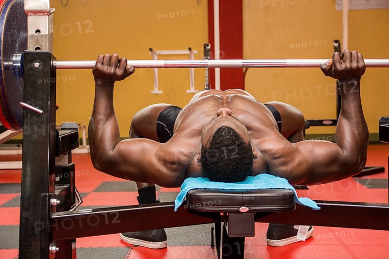 Hunky muscular black bodybuilder working out in gym, exercising pecs on bench with barbell