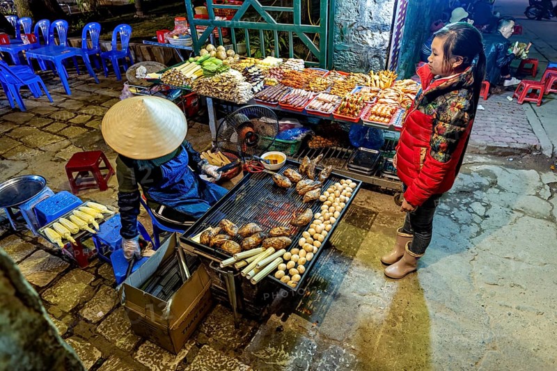 A busy street market with a stall selling grilled food surrounded by visitors, restaurant in the streets of Sa Pa in Vietnam