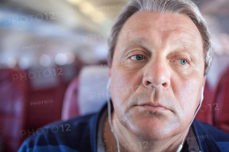 Close-up shot of mature man listening to music in headphones during traveling by plane. He looking distracted