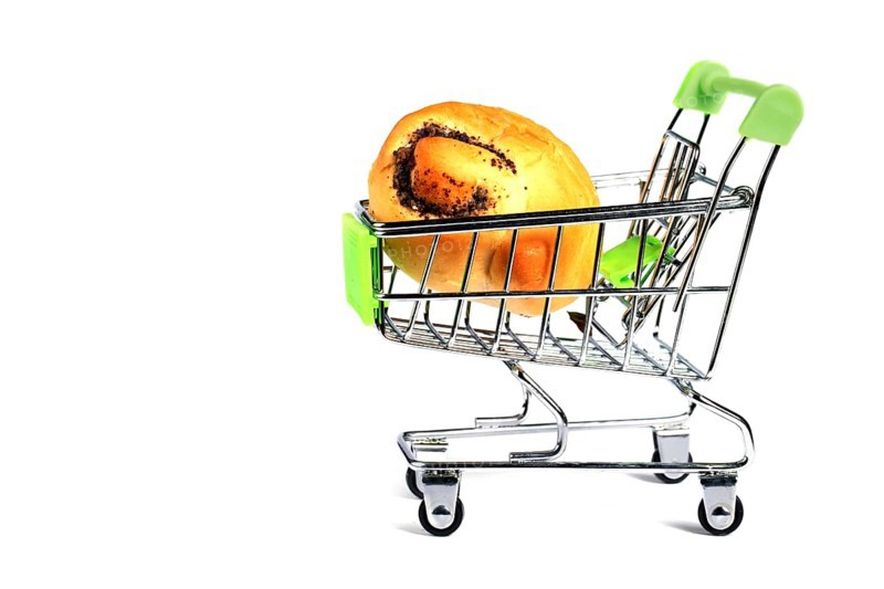 Miniature supermarket trolley with a bread roll on a white background