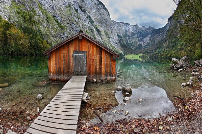 Cloudy day at Lake Koenigssee. Boathouse connected to the coast wooden decking. Clouds and mountains reflected in the water