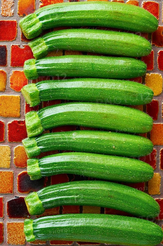 Mini zucchini vegetables in a row on red brown tiles table