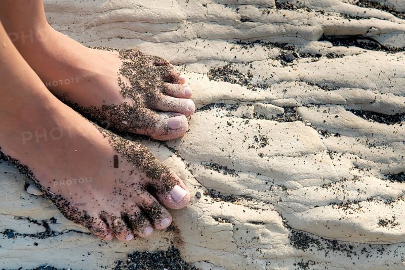 Unrecognised beautiful female food with beach sand on a white beach rocky surface