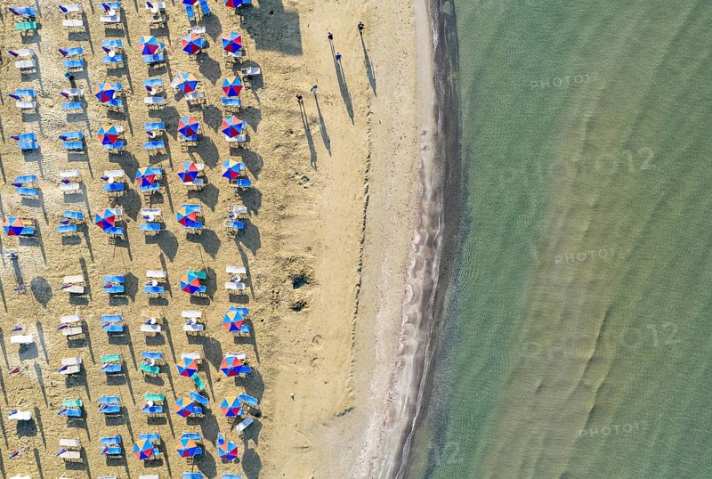 Aerial view of sandy beach with colorful umbrellas, people walking in the bay with transparent blue water at sunny day in summer. Larnaca, Cyprus travel