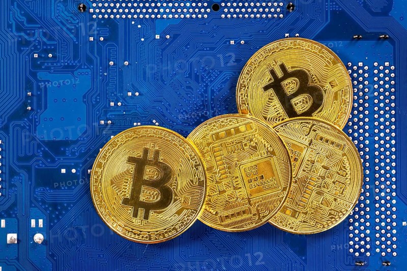 Virtual cryptocurrency money Bitcoin golden coins on a computer printed circuit board PCB. The future of money. Computational equipment. Blue mother board. Shot directly from above