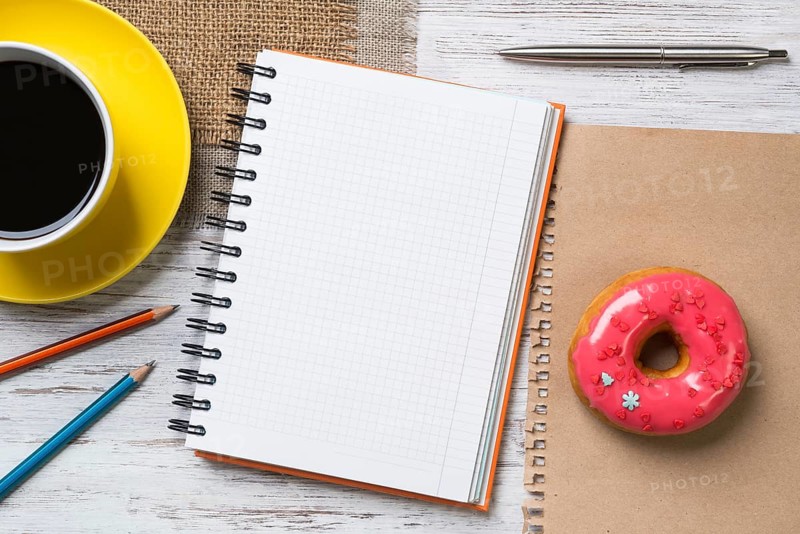 Opened notepad and cup of coffee with donut on wooden table