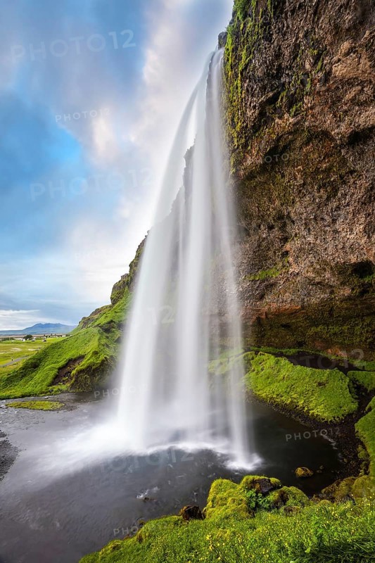 Sunny day in Iceland. Seljalandsfoss waterfall in July. Passage under the waterfall