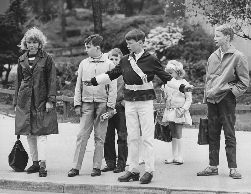 Junior safety patrol in the 1960s. A teenage boy stands with his arms out and signals to the pedestrians to stop at the crosswalk. When the cars have passed or stopped, the children can walk across the street. Being part of the Junior safety patrol was voluntary for the school students and the reward was sometimes to go on shorter trips and excursions. Nowadays, the operation is closed in many municipalities. Sweden 1964