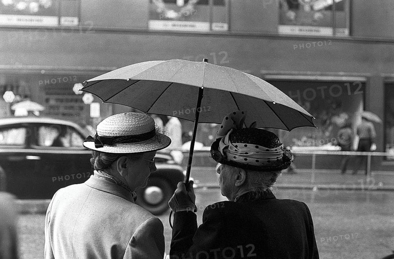 Umbrellas in the 1950s. The rain is pouring and two elderly ladies is seen holding an umbrella over themselves. It's a rainy day in Stockholm Sweden 1953. ref 1, 2