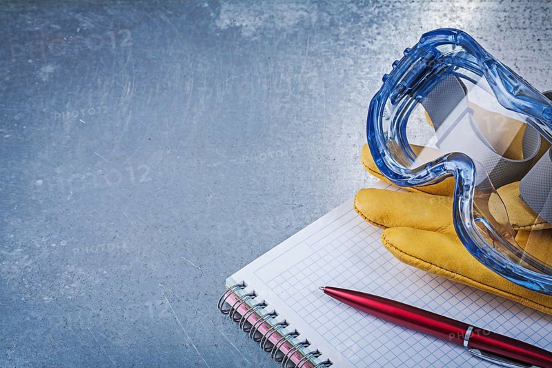 Plastic goggles leather gloves copybook pen on metallic background