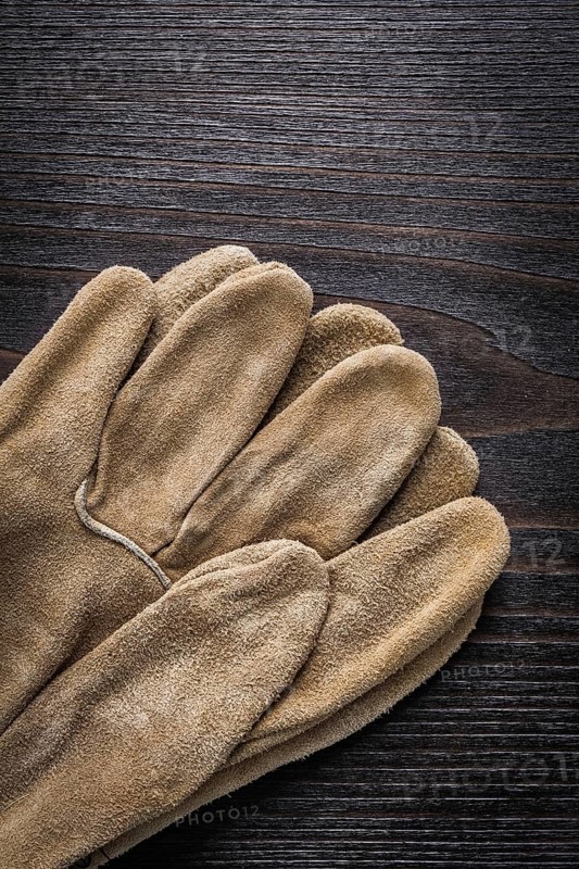 Leather working gloves on vintage wooden board vertical version construction concept