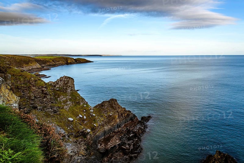 Scenic view of cliffs in Old Head of Kinsale peninsula in Ireland with green hills at sunset