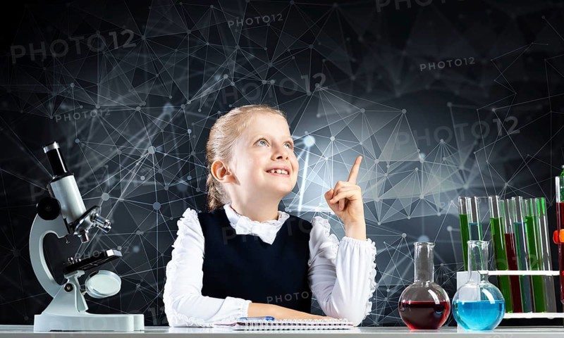 Little girl scientist sitting at desk in elementary science class. Research and education in school. Chemical laboratory with microscope, flasks and test tubes. Happy schoolgirl finger pointing up