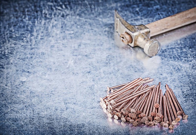 Vintage claw hammer stack of copper construction nails on metallic background
