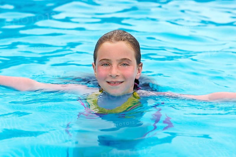 Blond kid girl swimming in the pool with sun tan red cheeks