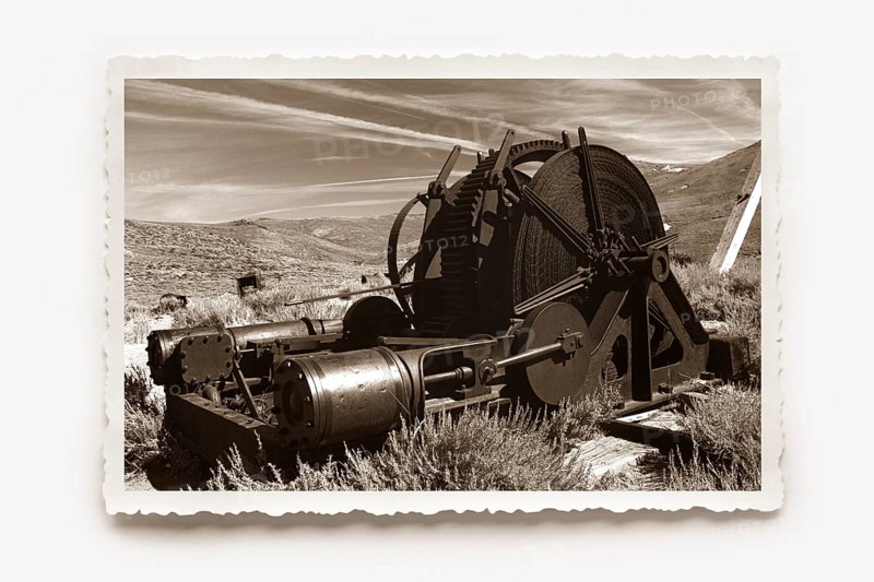 A monstrous old machine used in gold mining, rusting away in the former gold mining town of Bodie. Photo in sepia tones with white jagged edge, reclining shadow. A monstrous, old machine used in gold mining rusting in the former gold mining town of Bodie. Photo in sepia tones, all around a white jagged edge in the character of old photos