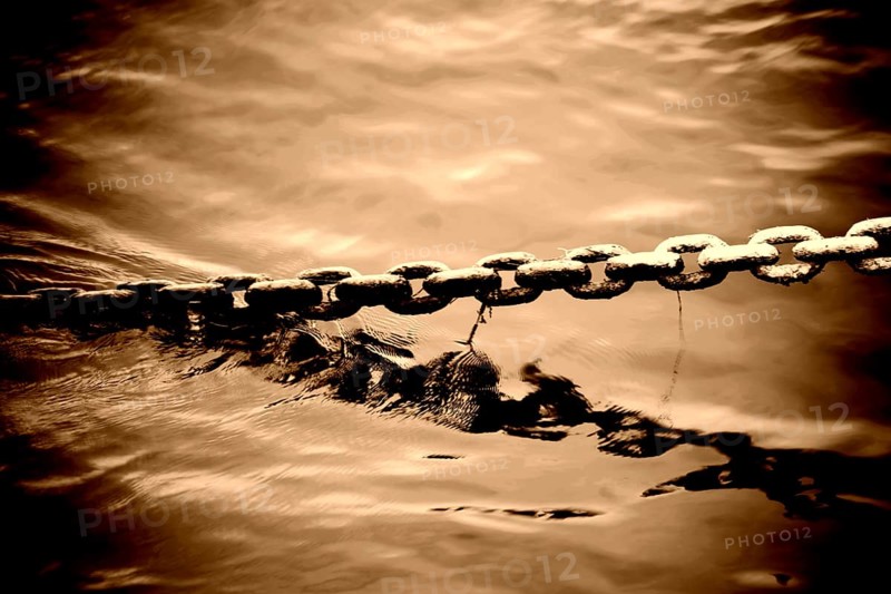 The bizarre and brute toning of an anchor chain protruding from a body of water
