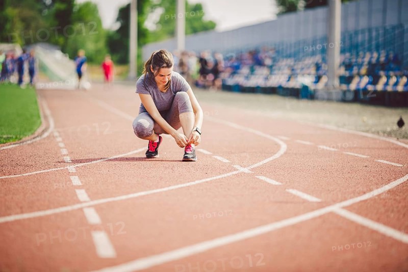 Theme sports and sportswear. A young Caucasian woman in uniform lacing shoelaces adjusting shoes sneakers on a treadmill track in a stadium