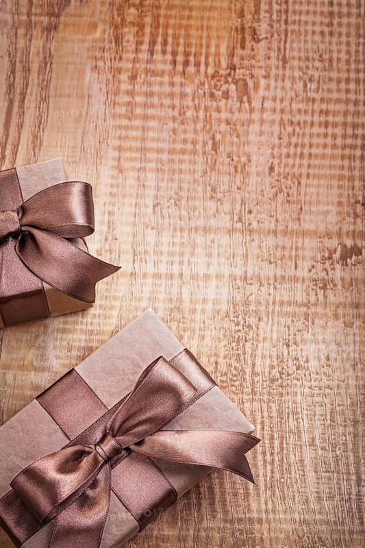 Conceptual copyspace photo two brown paper giftboxes with ribbons on vintage wooden board
