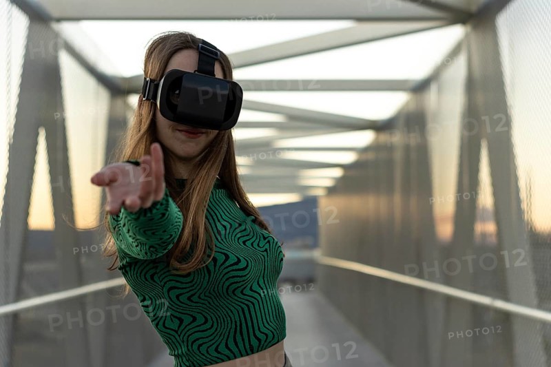 Young hispanic woman wearing in virtual reality goggles, touch something like push click on button, pointing at floating virtual screen outdoors. People sincere emotions, lifestyle concept