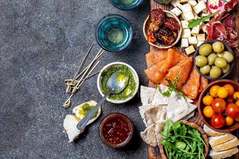 Antipasto. Wine set appetizer. Ham serrano, smoked salmon, dried and fresh tomatoes olive cheese, wine on board. Top view, gray cncrete background
