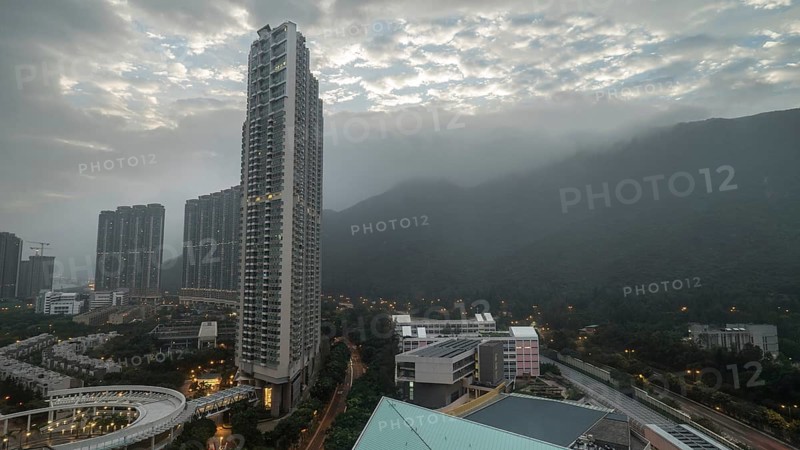 Cloudy sky over Hong Kong. Evening cityscape with high-rise buildings and green mountain