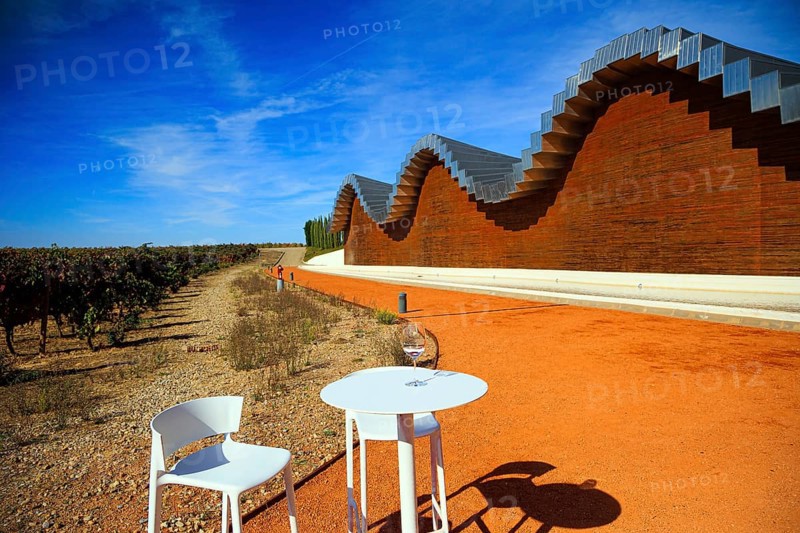 Table and chairs for tourists. Fragment of the facade. Wave-shaped winery roof. Winery - bodega Bodegas Ysios. Journey to the warm Spanish autumn. The sunset