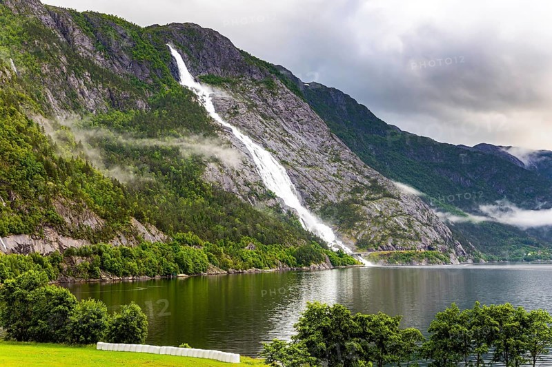 Magnificent giant picturesque Langfossen waterfall and flows into the Acre Fjord. Majestic natural phenomenon. Rainy cold July in Norway