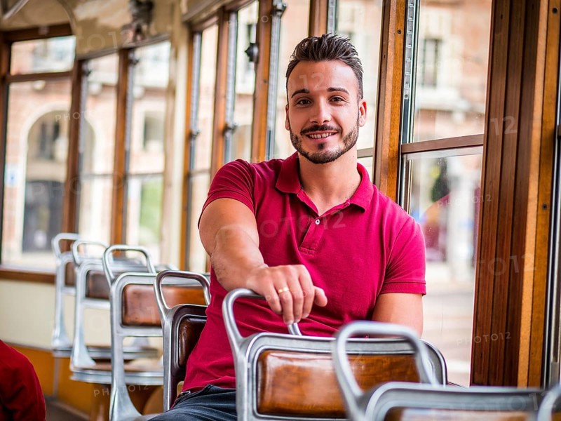 Young handsome man riding on tram or old bus in city, wearing polo shirt