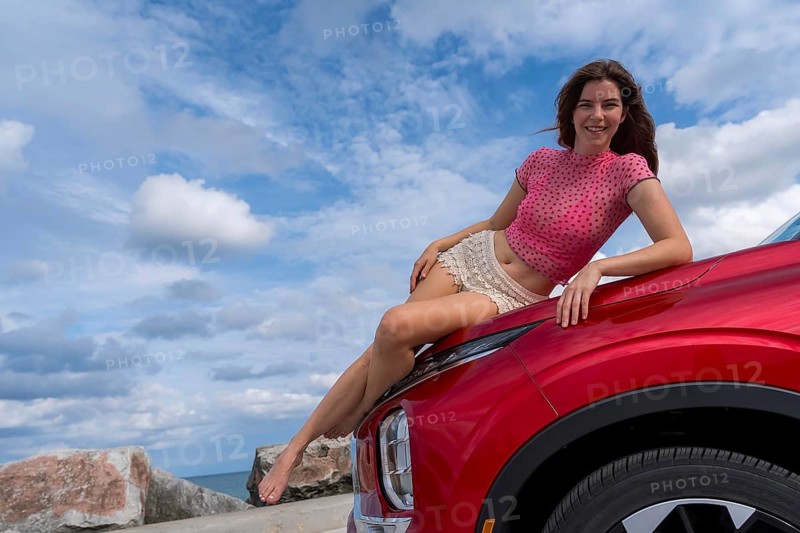 A gorgeous redhead model sits confidently on the hood of her car, soaking in the summer breeze as she embarks on an exciting cross-country adventure, the open road stretching ahead with endless possibilities, Milwaukee, United States of America