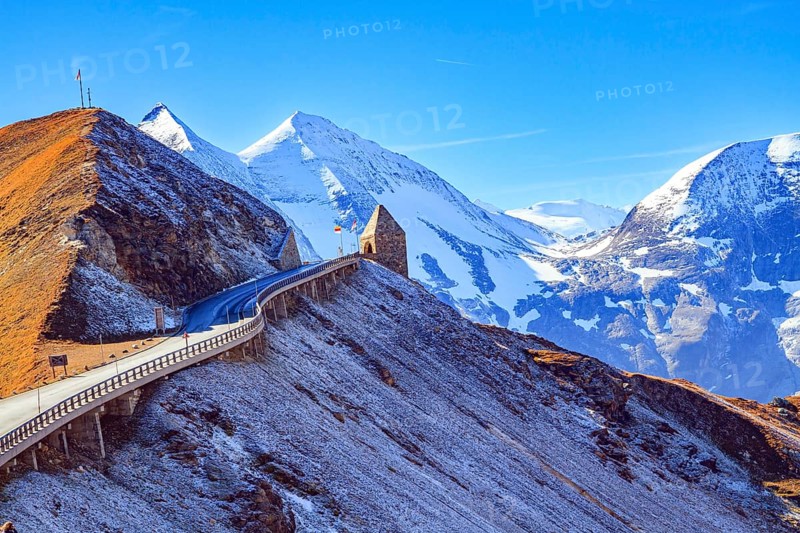 The famous panoramic mountain road Grossglocknerstrasse. Snow-capped mountain peaks are covered with clouds. Stone lookout tower at a sharp turn