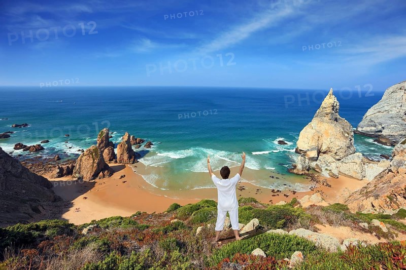 Small beautiful beach on the Atlantic coast. Middle-aged woman dressed in white doing yoga. The seaside resort of Sintra