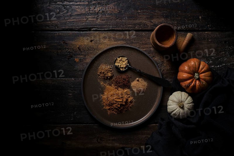 Top view of various ground handfuls of pumpkin spices on dishware and spoon at wooden plank table