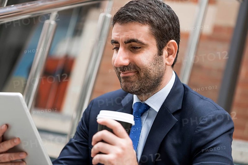 Confident businessman sitting on steps with tablet and coffee