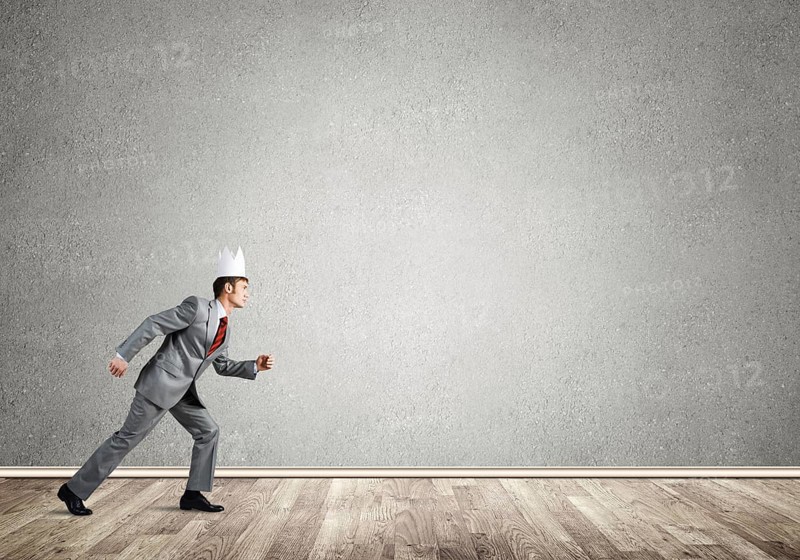 Young handsome businessman wearing white paper crown running in a hurry