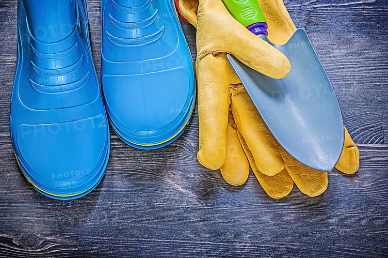 Leather safety gloves metal hand spade waterproof rubber boots on wooden board agriculture concept