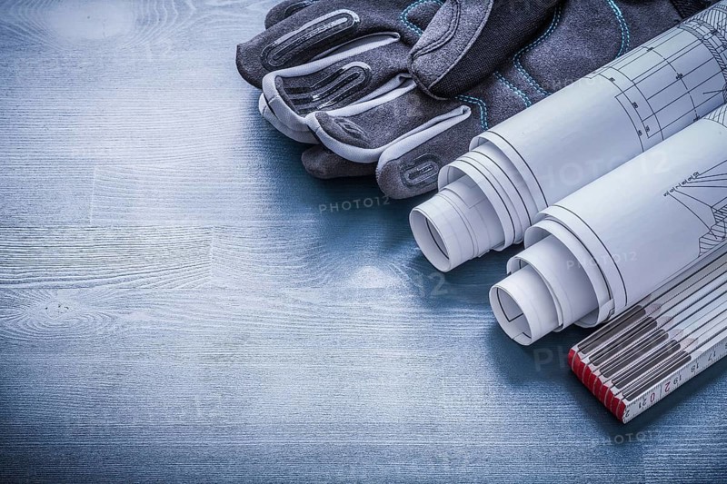 Rolled blueprints wooden meter and protective working gloves