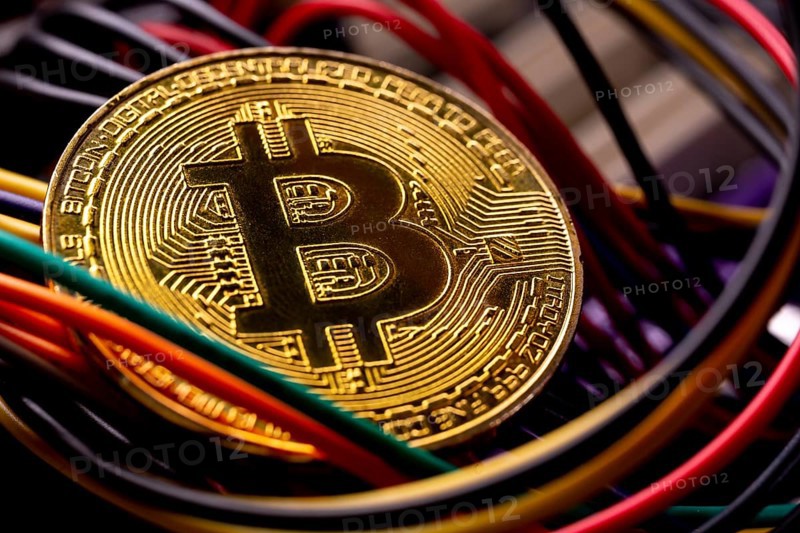 Virtual cryptocurrency money Bitcoin golden coin on a computer printed circuit board PCB surrounded by different colorful cables. The future of money. Computational equipment