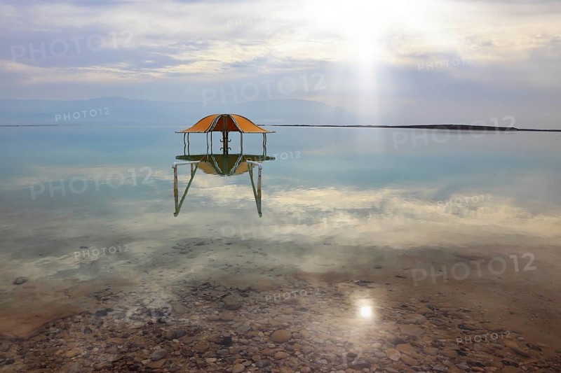 Medical beach on the Dead Sea, Israel. Round gazebo in the water near the water's edge. Cloudy sky reflected in water