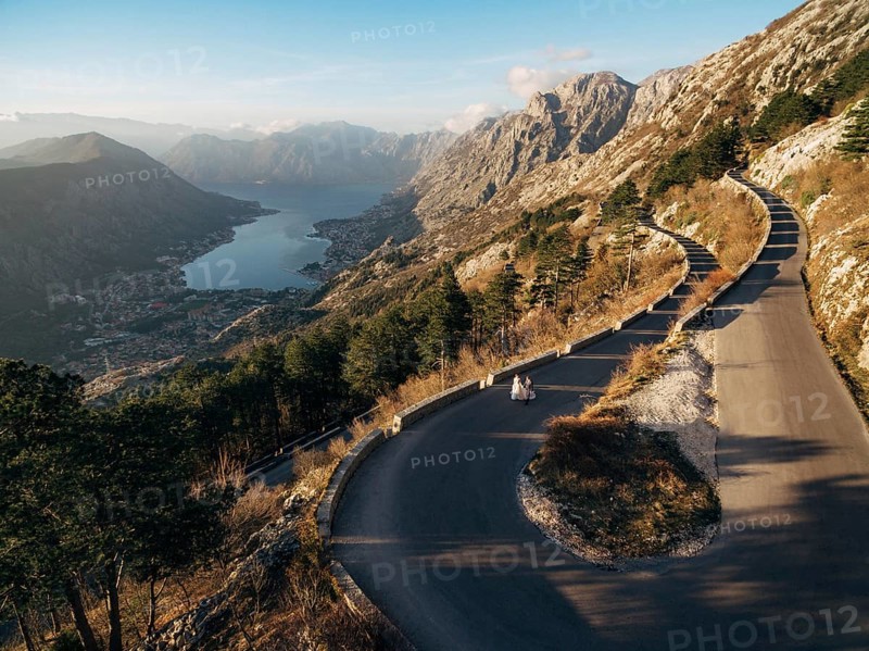 Bride and groom are walking along a high-mountain asphalt road over the bay.