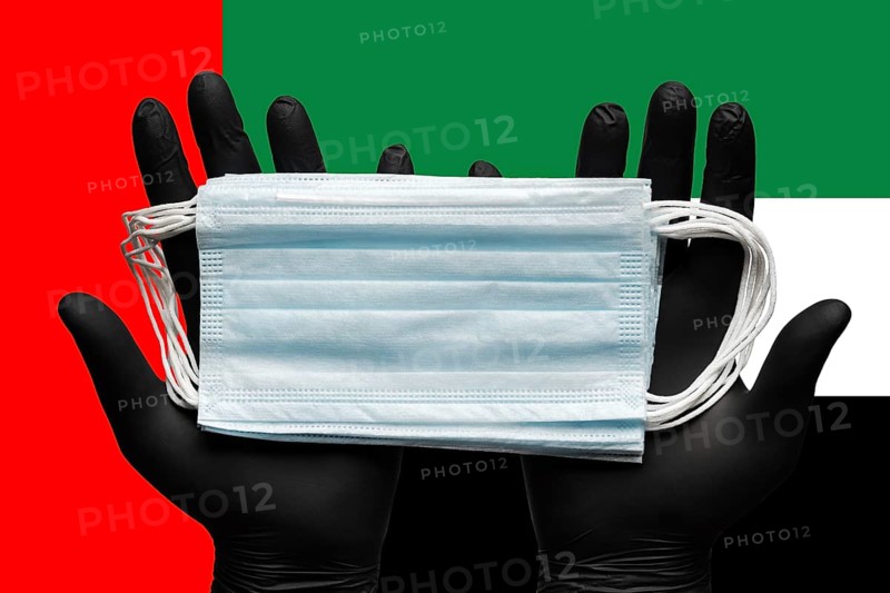 Doctor holds medical face mask in hands in black gloves on background colors national flag of United Arab Emirates UAE. Concept pandemic insurance coronavirus, quarantine, outbreak airborne diseases