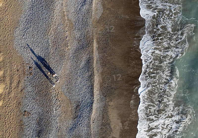 Aerial drone point of view of person walking on sand in a beach. Stormy waves idyllic beach in winter