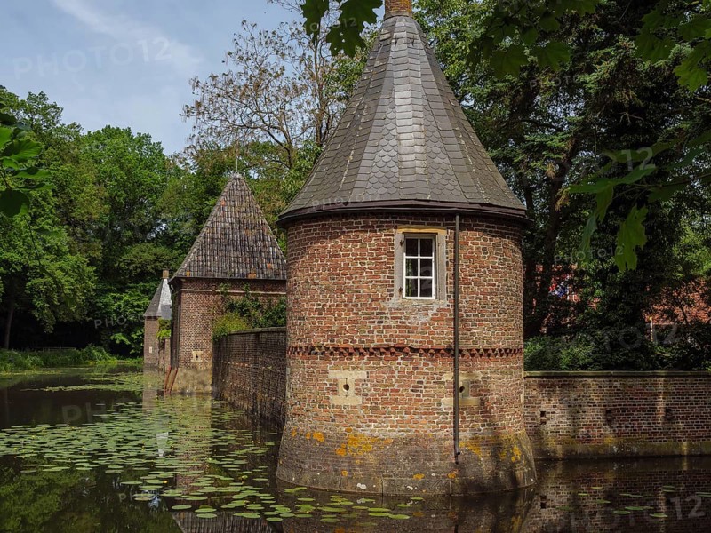 Brick building with towers reflected in a pond covered with water lilies, ochtrup, münsterland, germany