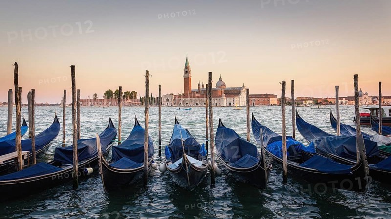 Gondolas moored docked on water in Venice. Gondoliers sailing San Marco basin waterway. San Giorgio Maggiore island with Campanile San Giorgio in Venetian Lagoon, blue clear sky, Veneto Region, Italy, Europe