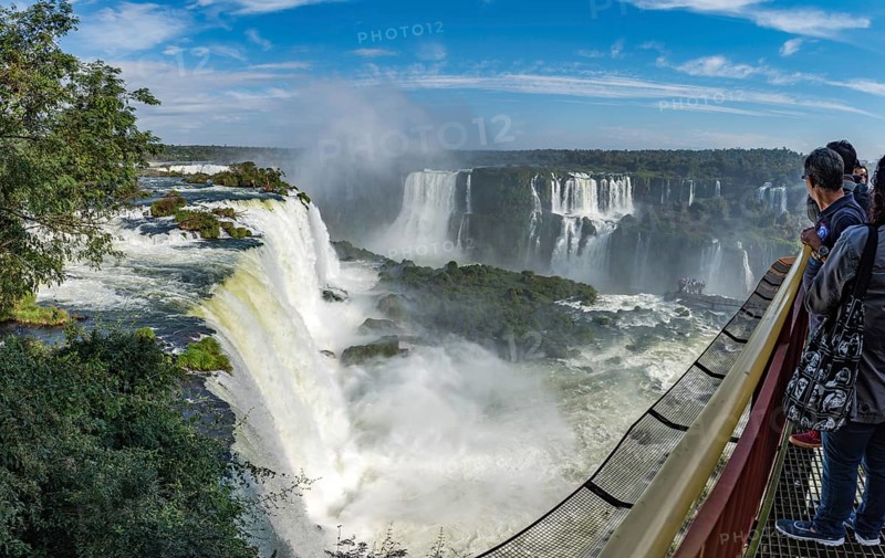 Foz do Iguacu, Brazil, july 9, 2016: Cataratas waterfalls view from the top with some rocks covered by grass in near the waterfall and bright blue sky as background, South America