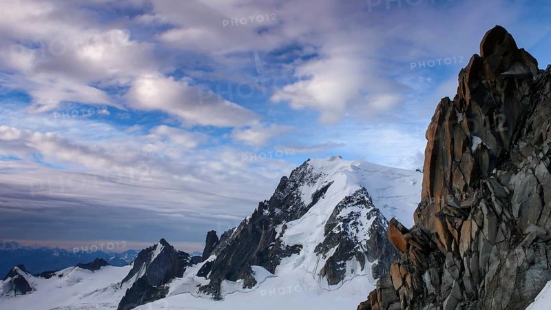 red granite rock needles with a great view of Mont Blanc in the background in the French Alps under a blue sky with white clouds