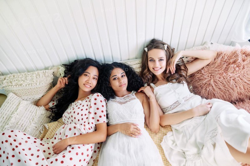 Beautiful multi ethnic girls have fun together, relax and lying on bed inside the camper van. Women friendship and females beauty concept. Caucasian, african american and asian girls posing at light interior