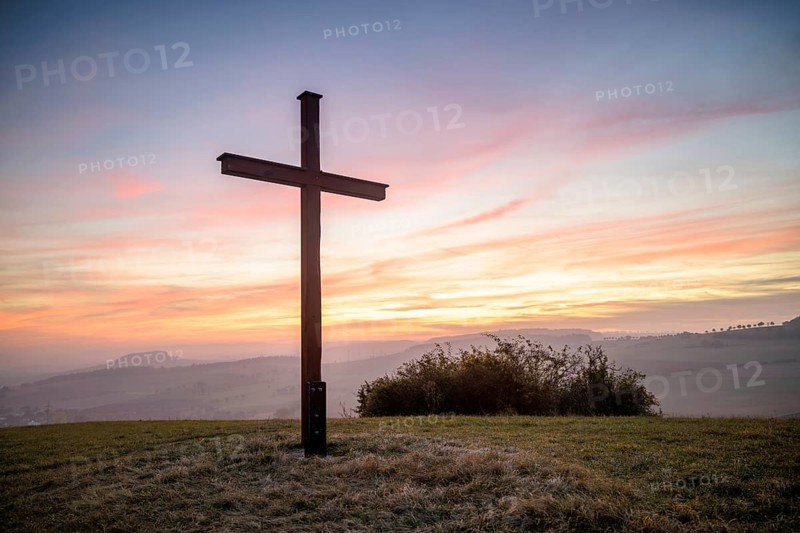 A cross stands in front of a colourful sunset in a peaceful landscape, Bisberg, Watterdingen, Hegau, Lake Constance region, Baden-Württemberg, Germany, Europe