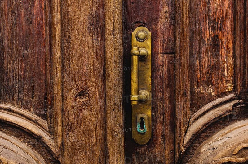 Vintage background. Brass-made old handle with Elements of an carved wooden door decorated with massive wooden simulating weaving. An old concept of old antiques. Varnished old mahogany